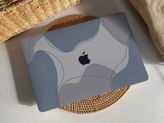 an apple laptop sitting on top of a wicker basket next to a woven pillow