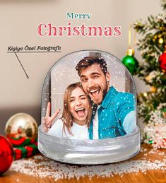 a couple under a snow globe with the words merry christmas on it and an ornament