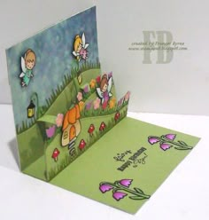 a pop up card with some little cartoon characters on the grass and flowers in the background