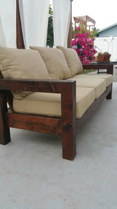 a wooden couch sitting on top of a cement floor next to a white drapes