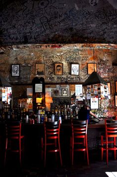 a bar with red chairs and graffiti on the wall behind it, in front of a man sitting at a bar