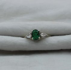 an emerald and diamond ring sitting on top of a white cloth