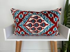 a red and blue pillow sitting on top of a white shelf next to a potted plant