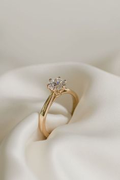 a gold ring with two diamonds sitting on top of white fabric, in the middle of an image