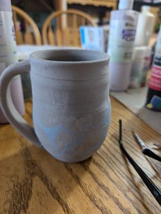 a cup sitting on top of a wooden table next to some scissors and other items