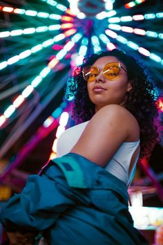 a woman wearing sunglasses standing in front of a ferris wheel with bright lights behind her