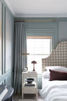 a bed sitting next to a window with a lamp on top of it in a bedroom