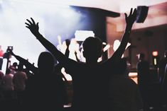 a person raising their arms in the air at a concert with other people standing around