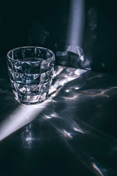 a glass sitting on top of a table next to a light shining in the dark