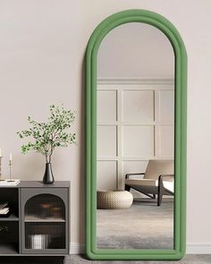 a large green mirror sitting on top of a wall next to a shelf with a vase