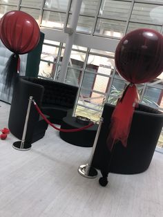 two red and black balloons tied to poles in an office lobby with large windows behind them