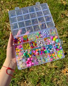 a person holding a plastic box filled with lots of beads and buttons on the grass