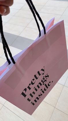 a pink paper bag with the words pretty things inside printed on it, held by someone's hand