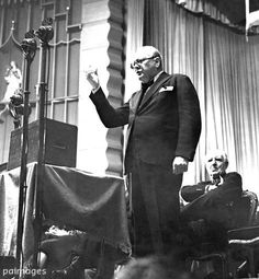 an old photo of a man standing in front of a podium with his hand up