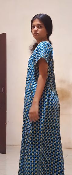 a woman standing in front of a door wearing a blue and yellow dress with circles on it