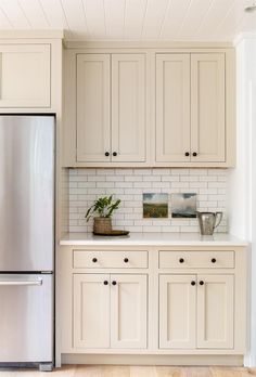 a kitchen with white cabinets and a silver refrigerator freezer next to a potted plant