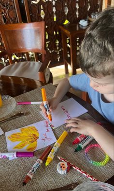 a young boy sitting at a table with some crayons and markers on it