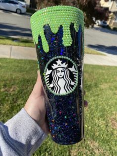 someone holding up a starbucks cup with green sprinkles and a black design on it