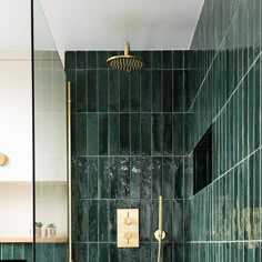 a green tiled bathroom with gold fixtures and black tiles on the shower wall, along with a brass faucet