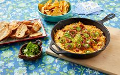 a skillet filled with cheesy hash browns next to some chips and salad