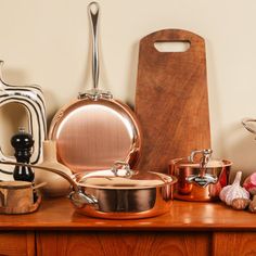 copper pots and pans are sitting on a wooden table next to a cutting board