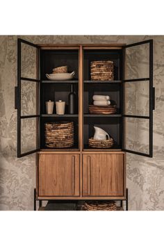 an open cabinet with baskets and dishes on it's sides, in front of a wallpapered background