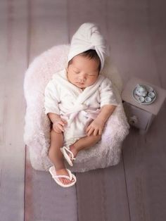 a baby in a white robe is laying down on a chair with shoes and a headband