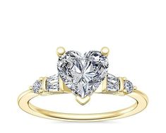 a heart shaped diamond ring with three stones on the band and two shoulders, set in yellow gold