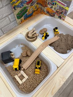 two trays filled with sand and toys on top of a table