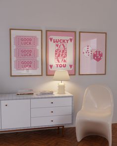 a white chair sitting next to a lamp on top of a wooden floor in front of two framed pictures