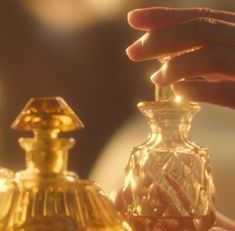 a person holding a small glass bottle next to a gold colored container with a diamond on it