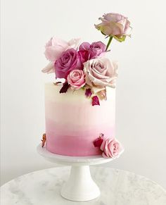 a pink and white cake with flowers on top sitting on a marble table in front of a white wall