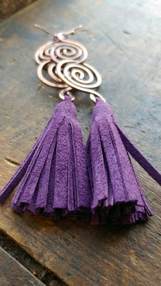 a pair of purple tasselled earrings sitting on top of a wooden table