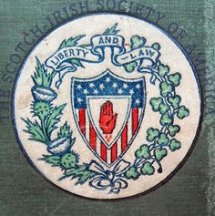 an emblem on the side of a building with green leaves and flowers around it that says liberty and anarchy