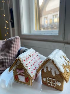 two gingerbread houses on a white plate with a window in the backround