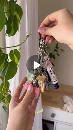 a person holding onto a key chain with various items attached to it, in front of a potted plant