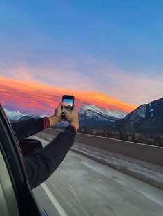 a man taking a photo with his cell phone while driving down the highway at sunset