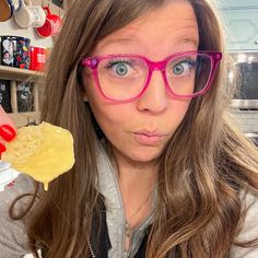 a woman in glasses is holding up a piece of food to her face and looking at the camera