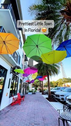 several colorful umbrellas hanging from the side of a building on a brick sidewalk next to parked cars