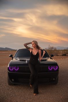 a woman leaning on the hood of a black sports car with her hands behind her head