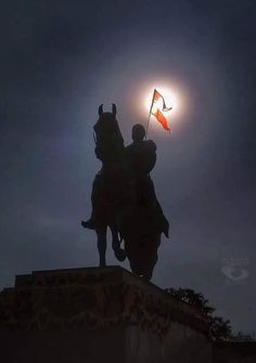 the sun is setting behind a statue of a man on horseback holding an orange flag