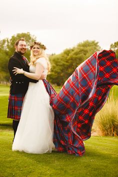 a man and woman dressed in scottish clothing posing for a photo with a tartan cloth draped over them