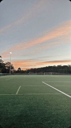 an empty tennis court with the sun setting in the background and trees on the other side