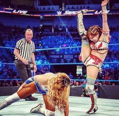 two women are wrestling in an arena while one woman is kneeling down on the ground