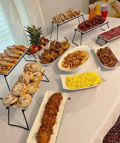 an assortment of food is displayed on a long table with white clothed tablescloths