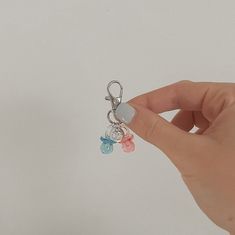 a hand holding a small key chain with charms attached to it's sides, on a white background