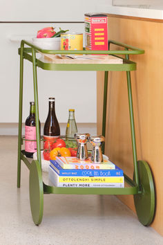 a green cart with books and drinks on it next to a counter top filled with food