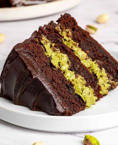 a slice of chocolate cake on a white plate with pistachios around it