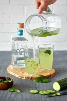 someone is pouring cucumber water into two glasses