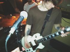 a young man playing an electric guitar in front of a microphone while another person watches